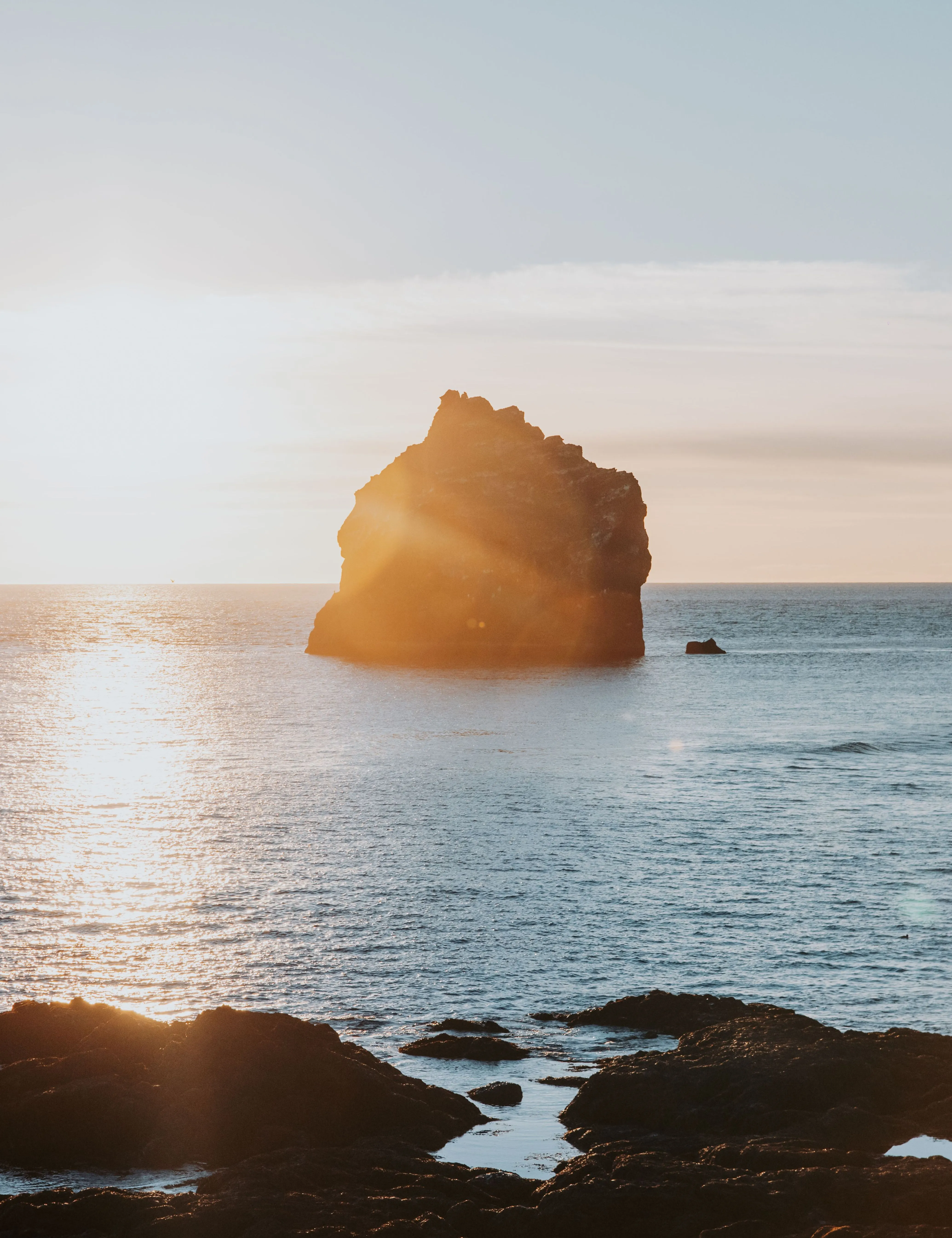 A small, jagged island just off the coast of Iceland's Reykjanes Peninsula as sunset is nearing, casting an orange glow on the water.