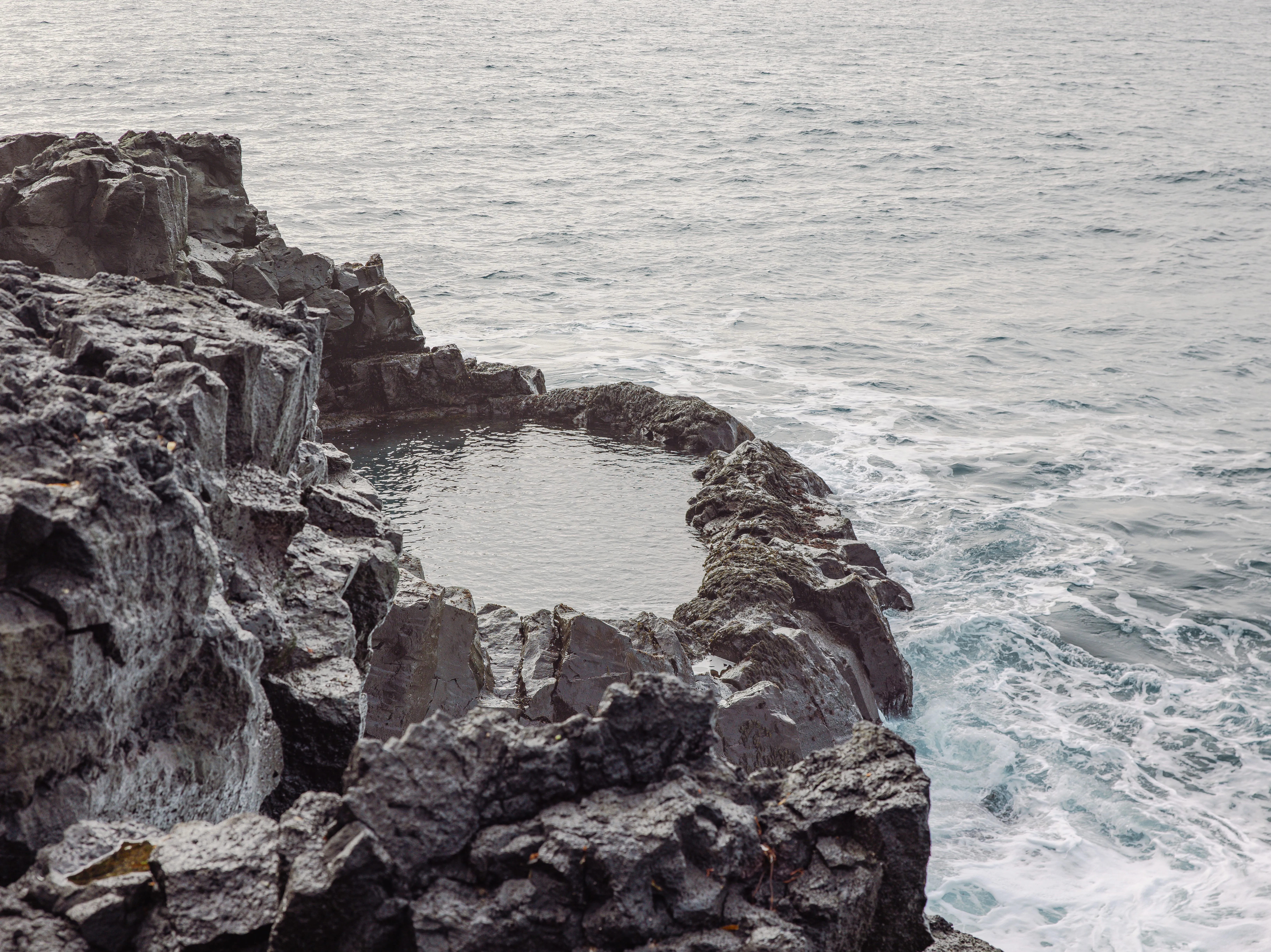 The ocean surrounds a small, natural pool cut out of rocky cliffs at the peninsula's edge.