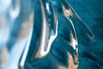 A vibrant blue glacial ice wall looks like ocean waves made of glass shimmering with warm, yellow sunlight.