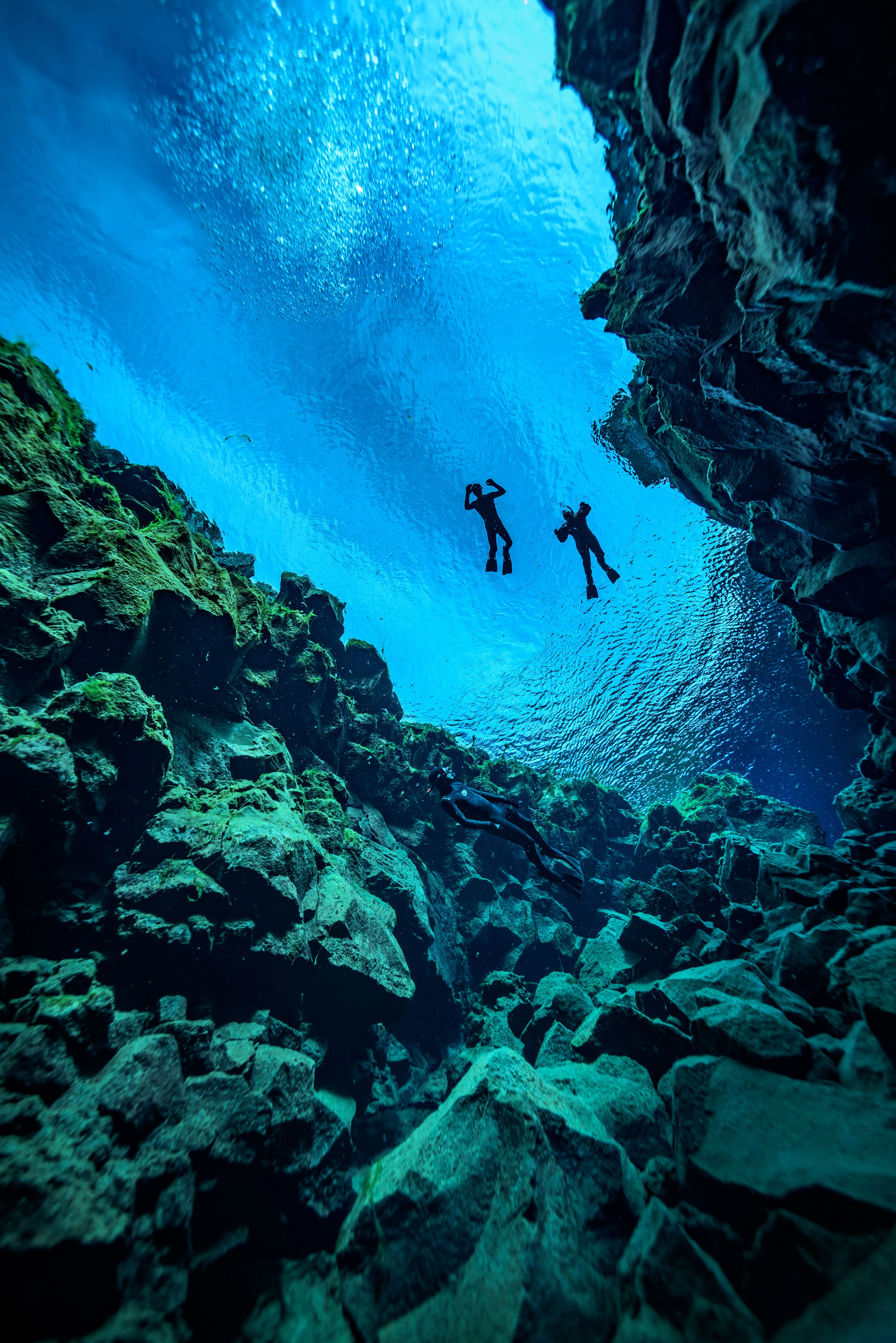 Sillouettes of two freedivers up on the surface of Silfra's vibrant blue waters between rocky fissure walls.