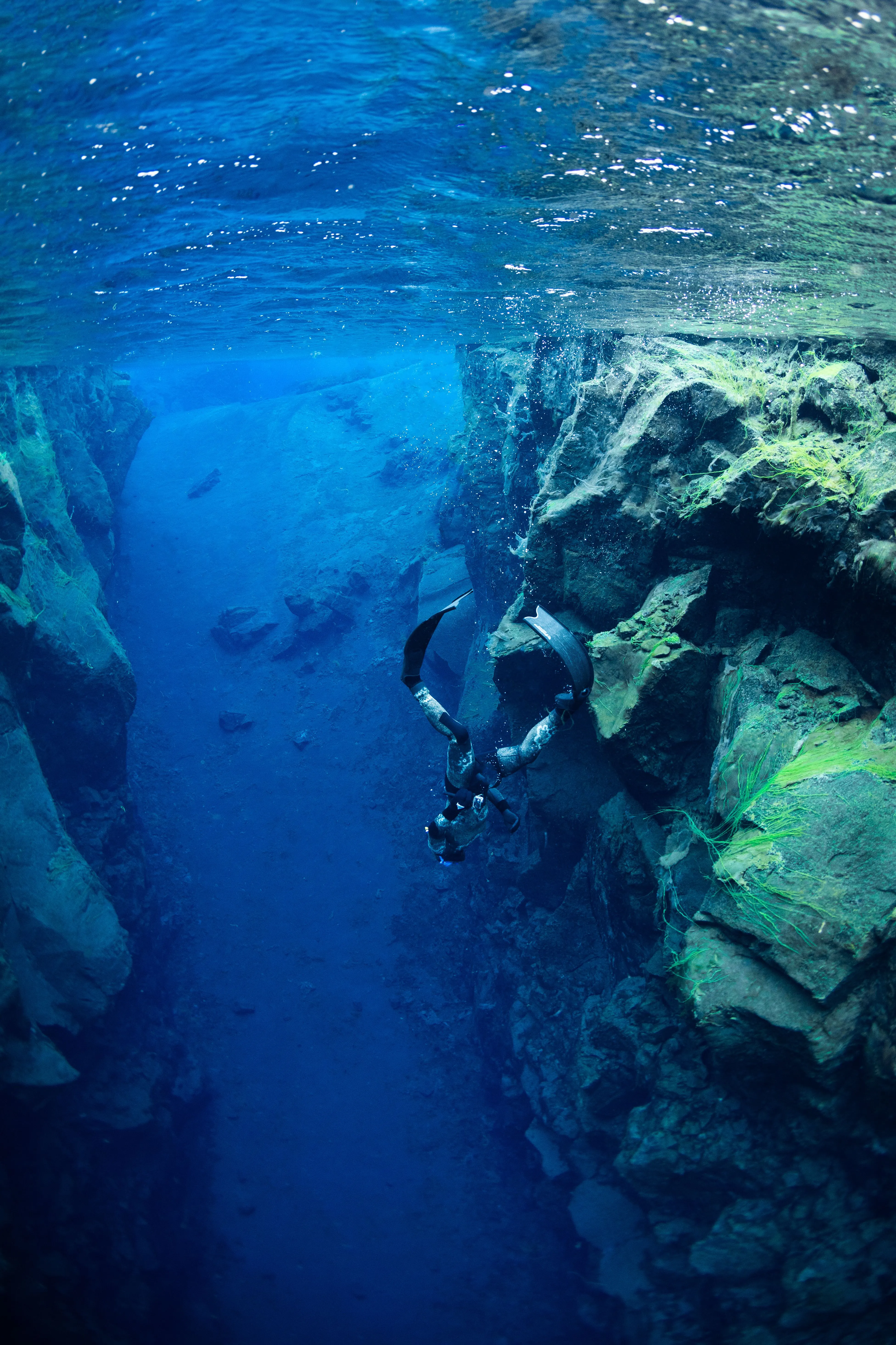 A freediver swimming down into a deep fissure with a sandy bottom.