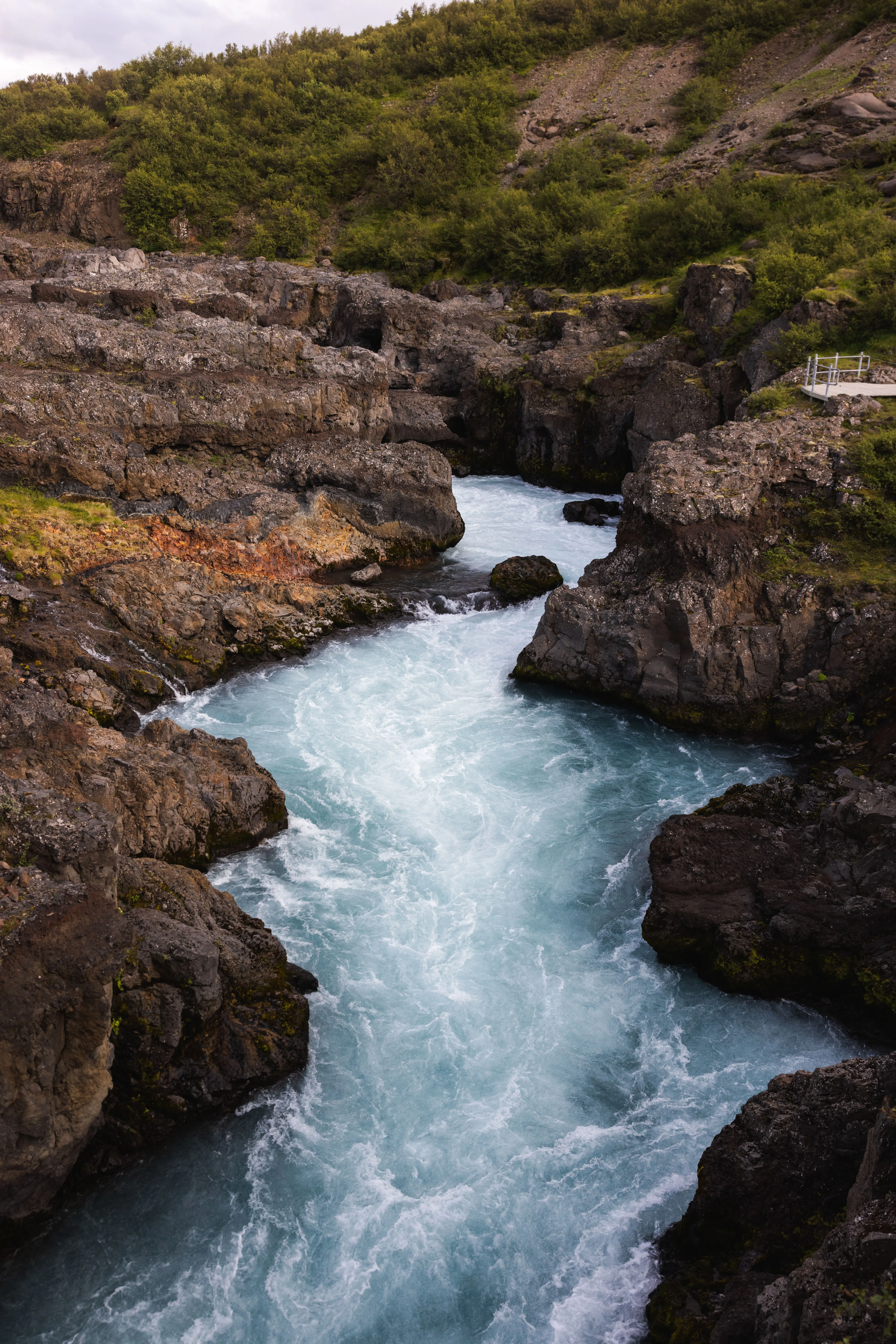 A Light blue waterfall cascades through a narrow gorge, its appearance more akin to tumultuous river rapids.
